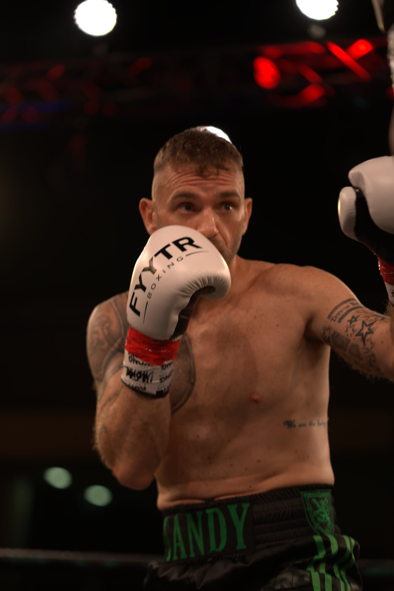 Boxer standing side on in a white vest and white boxing gloves
